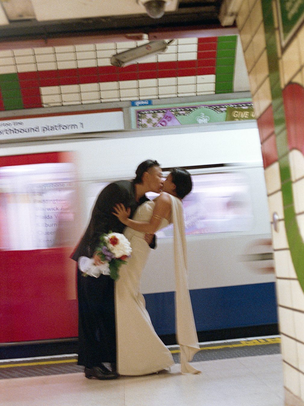 Jasper and Moe kissing on a London Underground platform as a train rushes past